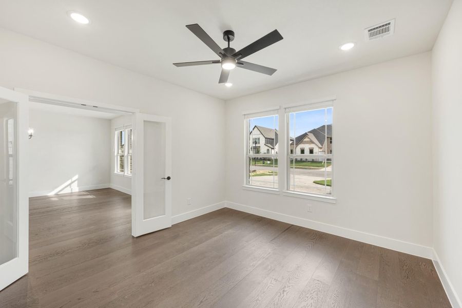 Empty room with dark hardwood floors, white walls, ceiling fan, and two windows with neighborhood view