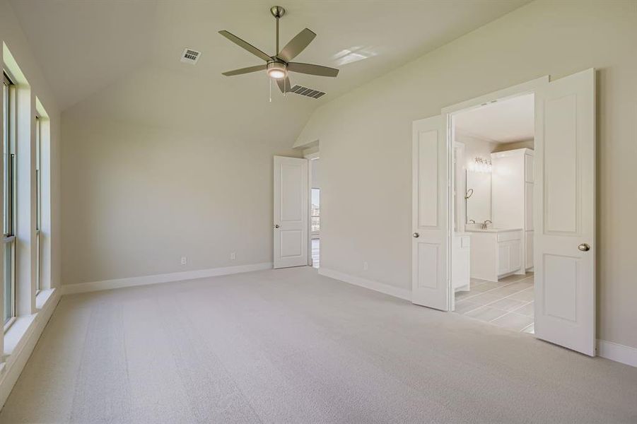 Unfurnished bedroom featuring vaulted ceiling, light colored carpet, ceiling fan, and ensuite bath