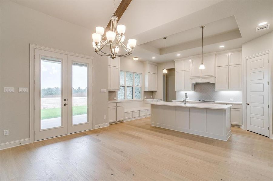 Kitchen with pendant lighting, light hardwood / wood-style flooring, a center island with sink, and a tray ceiling