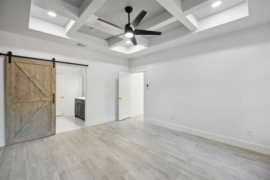 Unfurnished bedroom featuring coffered ceiling, light hardwood / wood-style flooring, ensuite bath, a barn door, and ceiling fan