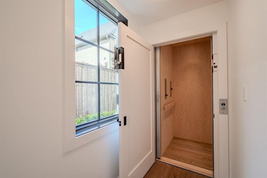 Doorway to outside with healthy amount of natural light, elevator, and wood finished floors Doorway to outside with healthy amount of natural light, elevator, and wood finished floors