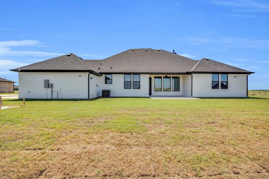 Rear view of house with central AC unit and a lawn