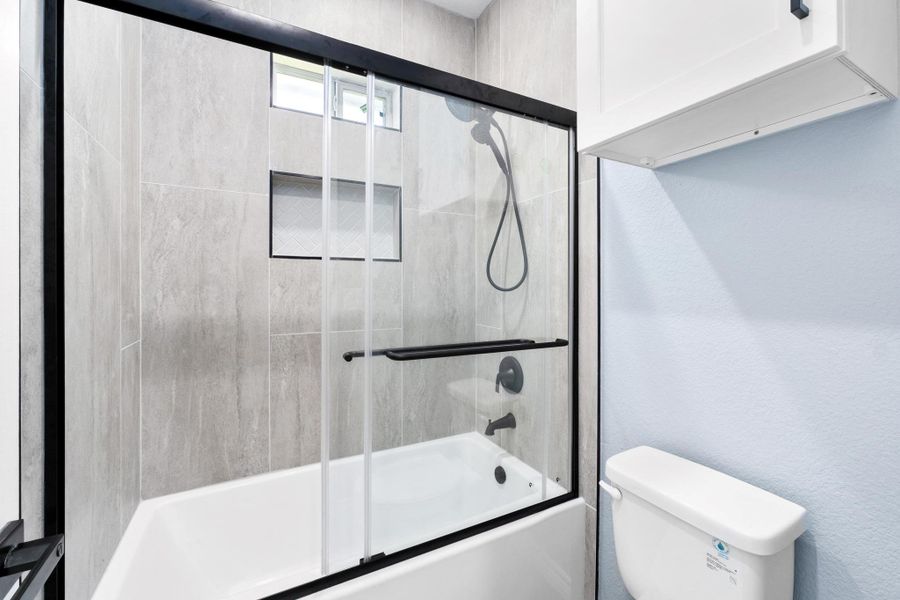 Bathroom featuring enclosed tub / shower combo and a textured wall Bathroom featuring enclosed tub / shower combo and a textured wall