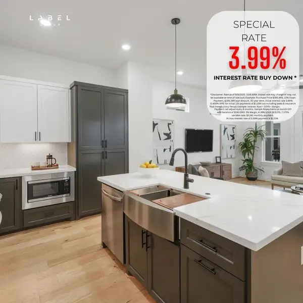 This modern kitchen features sleek black and white cabinetry, a central island with barstools, and pendant lighting. The open layout flows into a dining area with a wooden table, and a staircase leads to the upper level. Large windows provide natural light, creating a bright and inviting space.