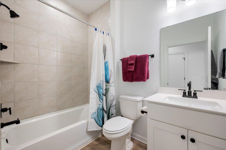 Full bath with vanity, shower / tub combo, a textured wall, and wood finished floors Full bath with vanity, shower / tub combo, a textured wall, and wood finished floors