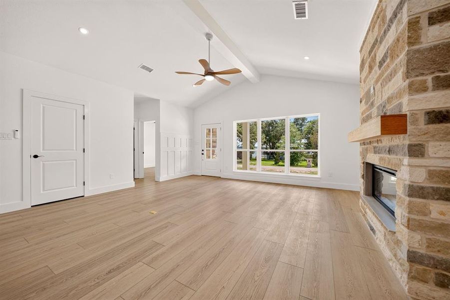 Spacious living area featuring wood-finish flooring, a stone-faced fireplace with a wood mantle, and a vaulted ceiling with exposed beam and ceiling fan