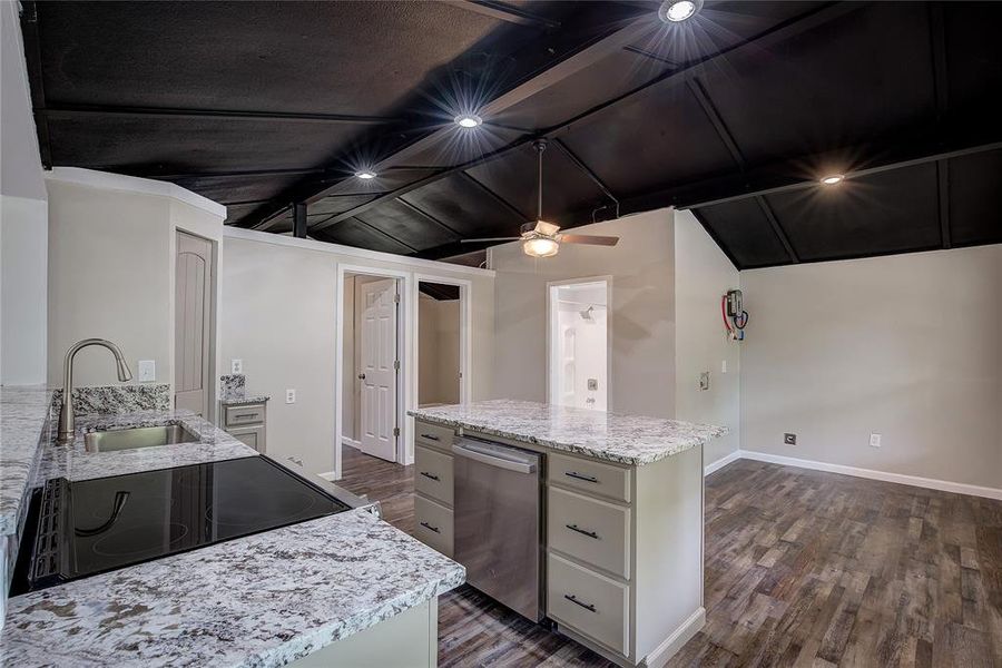 Kitchen featuring stainless steel dishwasher, light stone countertops, sink, and vaulted ceiling with beams