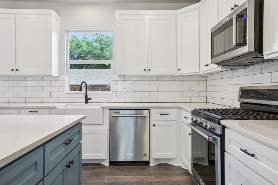 Kitchen with appliances with stainless steel finishes, white cabinetry, decorative backsplash, and light stone countertops