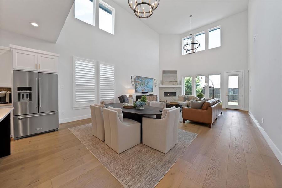 Spacious open-concept living area featuring a two-story ceiling, light wood-finish flooring, and multiple windows Spacious open-concept living area featuring a two-story ceiling, light wood-finish flooring, and multiple windows