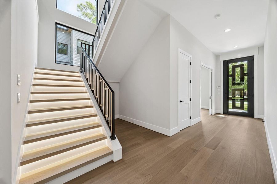 Guests are welcomed by a dramatic entry marked by a sleek glass-and-metal front door that opens to a spacious, sunlit corridor. The staircase itself is a design highlight, featuring illuminated stair treads that provide both ambiance and safety. A modern iron railing and expansive glass-pane windows with a lighted accent wall complete the dramatic architectural statement. Guests are welcomed by a dramatic entry marked by a sleek glass-and-metal front door that opens to a spacious, sunlit corridor. The staircase itself is a design highlight, featuring illuminated stair treads that provide both ambiance and safety. A modern iron railing and expansive glass-pane windows with a lighted accent wall complete the dramatic architectural statement.