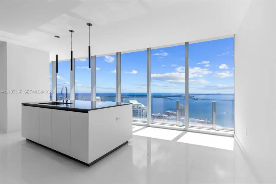 Kitchen island with a dark countertop and integrated sink, complemented by three modern pendant lights and floor-to-ceiling windows featuring coastal scenery