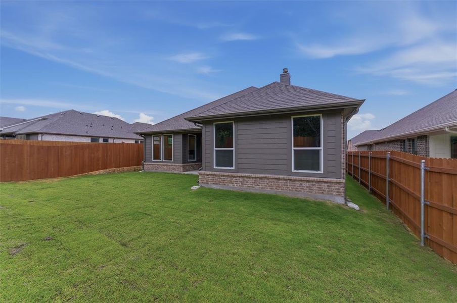 Expansive green lawn surrounds the property, featuring dark gray horizontal siding and a brick base