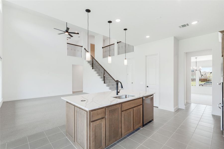 Kitchen island with quartz countertop, sink, and wood cabinets, open to two-story living area with staircase and pendant lights