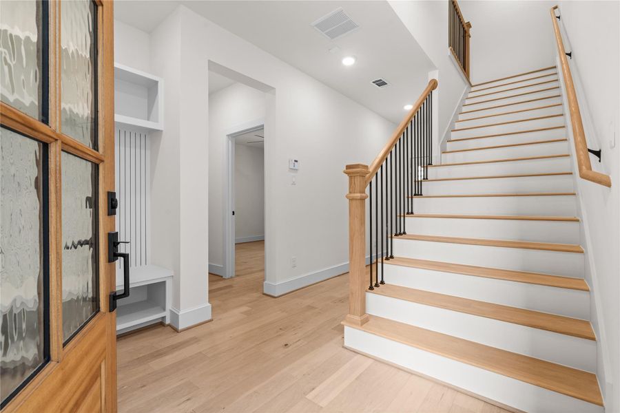 A bright entryway with a wooden front door, leading to a staircase with wooden steps and a metal railing. The space features white walls, engineered wood floors, and modern decor, creating a welcoming and contemporary atmosphere. A bright entryway with a wooden front door, leading to a staircase with wooden steps and a metal railing. The space features white walls, engineered wood floors, and modern decor, creating a welcoming and contemporary atmosphere.
