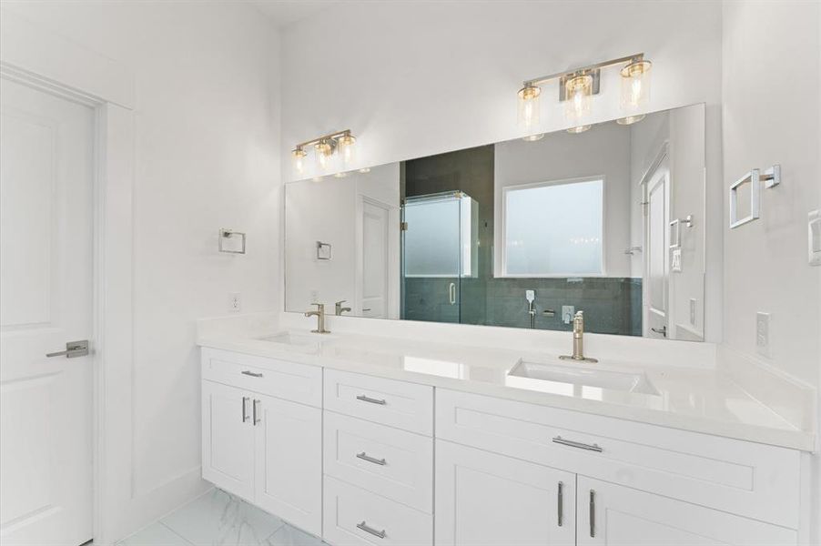 This bathroom features a modern design with a sleek double vanity and ample storage space. It has a large mirror above the sinks, stylish lighting fixtures, and a glass-enclosed shower, creating a bright and spacious feel.