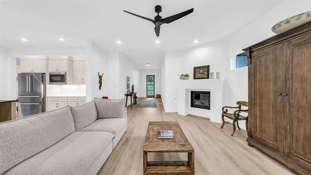 Living area featuring recessed lighting, light wood-type flooring, ceiling fan, a glass covered fireplace, and baseboards Living area featuring recessed lighting, light wood-type flooring, ceiling fan, a glass covered fireplace, and baseboards