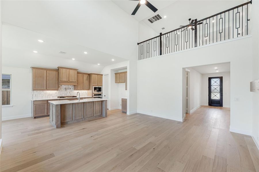 Open-concept living area with kitchen island, wood cabinets, high ceilings, and second-floor iron railing balcony