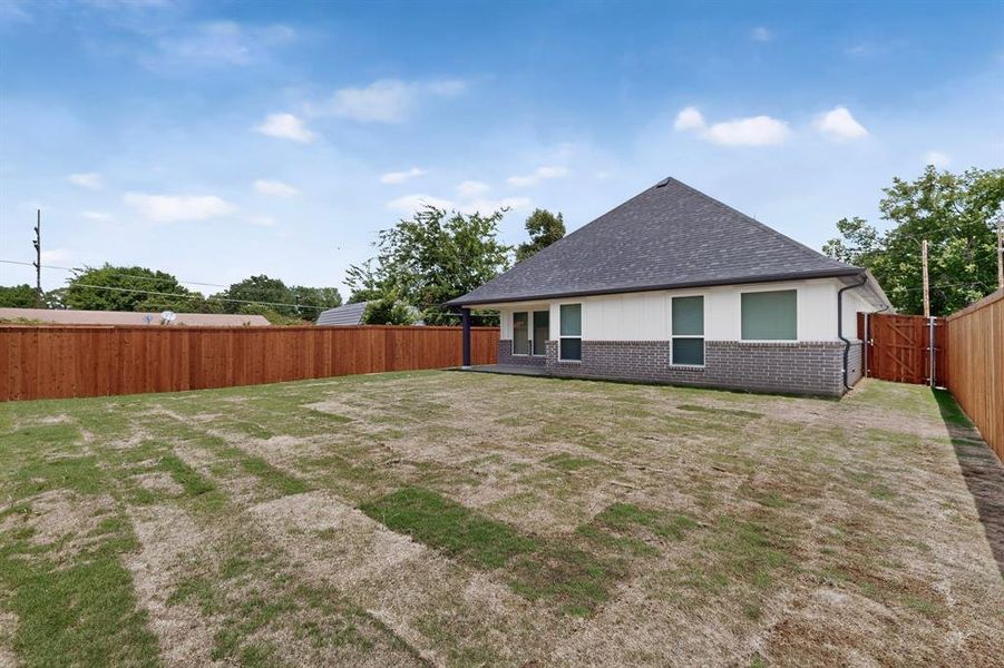 Spacious backyard featuring a new privacy fence, partial brick exterior, white siding, a shingled roof, and a side gate