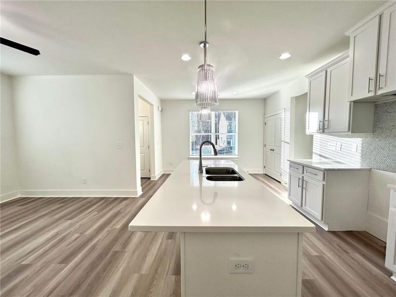 Kitchen with hanging light fixtures, sink, a kitchen island with sink, backsplash, and light wood-type flooring