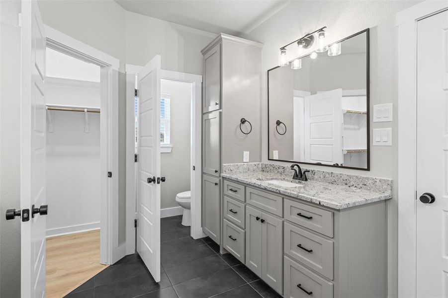 Full bathroom with a spacious closet, vanity, and dark tile patterned floors Full bathroom with a spacious closet, vanity, and dark tile patterned floors