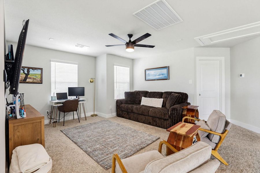 Carpeted bonus room featuring a ceiling fan, multiple windows with blinds, a white paneled door, and neutral wall tones