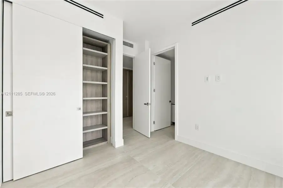 Minimalist interior featuring wood-finish flooring, recessed linear ceiling diffusers, sliding panel doors, and built-in shelving with wood-tone interior Minimalist interior featuring wood-finish flooring, recessed linear ceiling diffusers, sliding panel doors, and built-in shelving with wood-tone interior