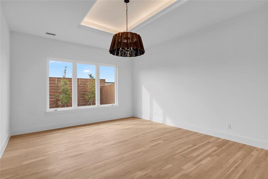 Unfurnished dining area with light wood-type flooring, hanging lights, and a tray ceiling Unfurnished dining area with light wood-type flooring, hanging lights, and a tray ceiling