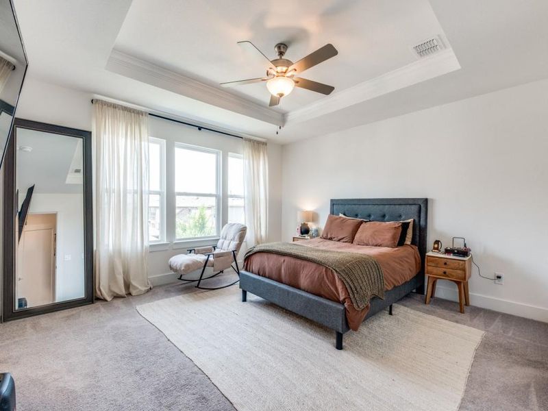 Bedroom with a raised ceiling, light colored carpet, crown molding, and a ceiling fan