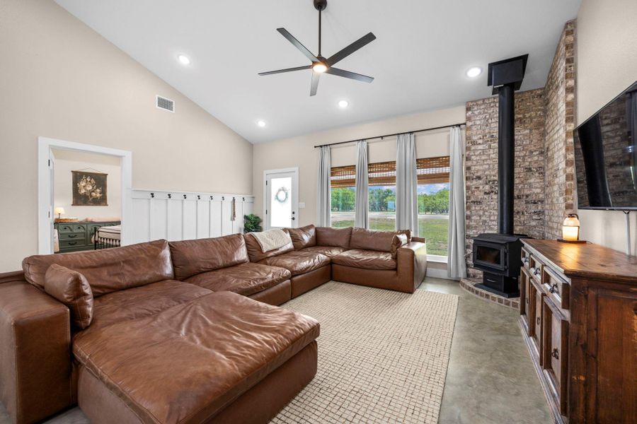 Living area featuring a wood stove, a ceiling fan, concrete flooring, vaulted ceiling, and recessed lighting