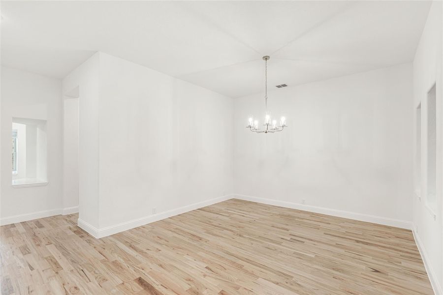 Empty dining room with light hardwood floors, white walls, and a chandelier overhead