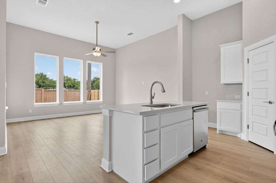 Kitchen with white cabinets, an island with sink, light wood-style flooring, ceiling fan, and stainless steel dishwasher