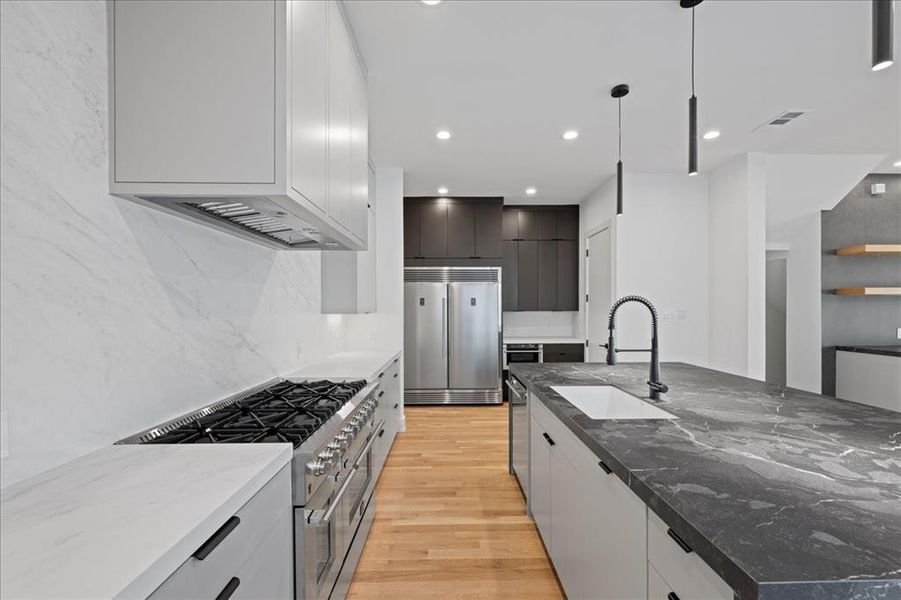 Kitchen with high end appliances, dark stone counters, light wood-style flooring, modern cabinets, and recessed lighting Kitchen with high end appliances, dark stone counters, light wood-style flooring, modern cabinets, and recessed lighting