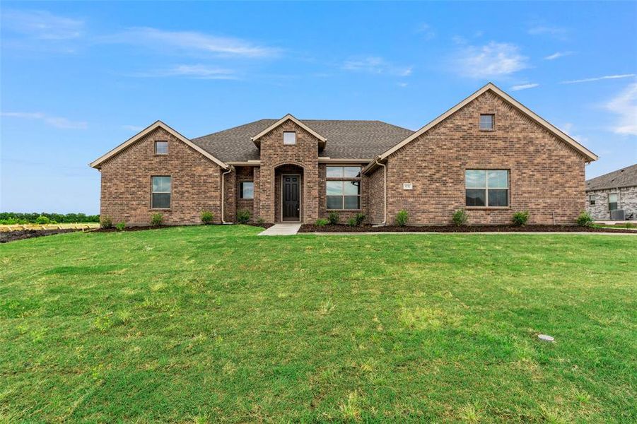 View of front facade featuring brick siding, a front yard, a shingled roof, and cooling unit