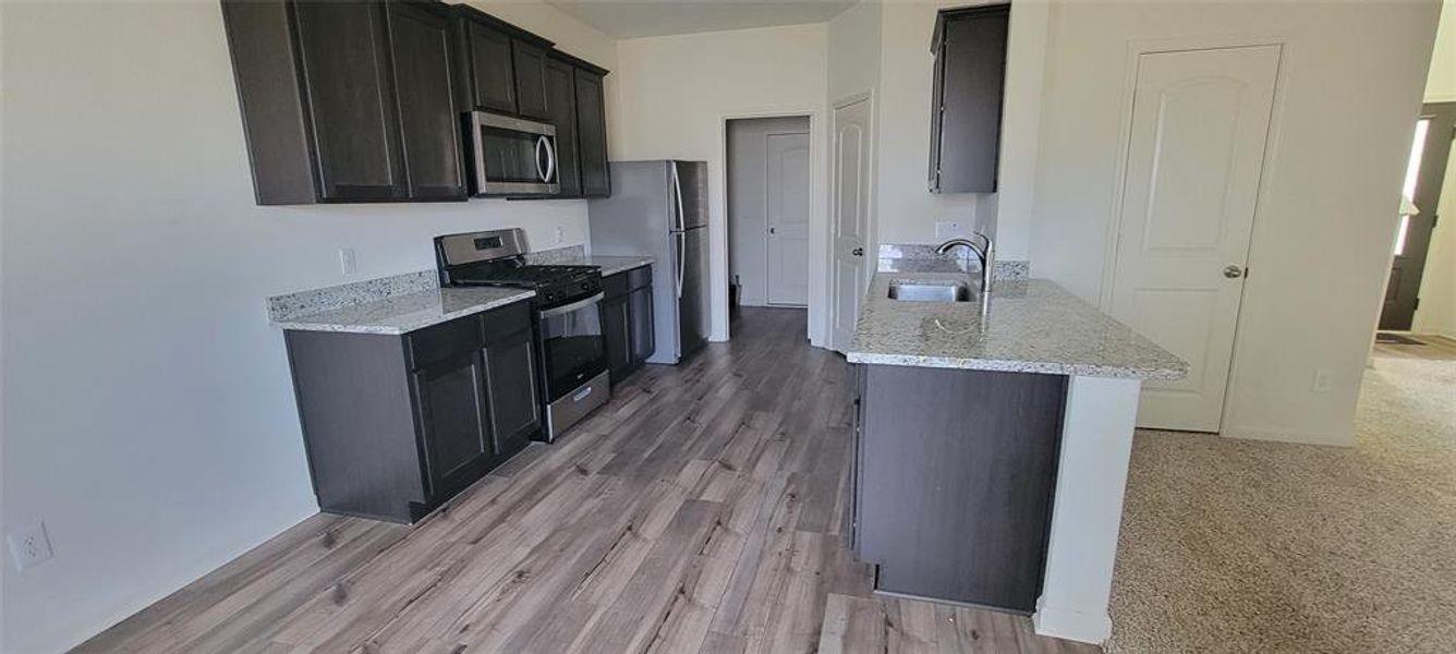 Kitchen featuring light stone countertops, sink, light wood-type flooring, and appliances with stainless steel finishes