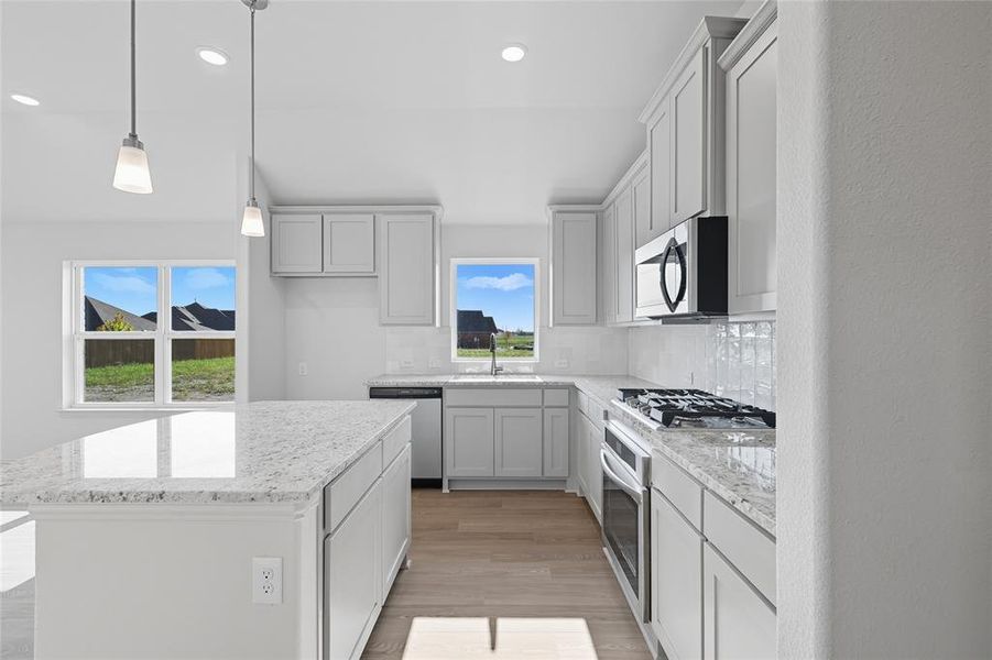Kitchen featuring light wood-style flooring, tasteful backsplash, recessed lighting, decorative light fixtures, and light stone countertops Kitchen featuring light wood-style flooring, tasteful backsplash, recessed lighting, decorative light fixtures, and light stone countertops
