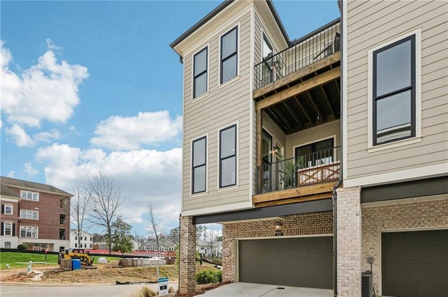 View of side of home featuring a balcony, brick siding, a garage, and concrete driveway