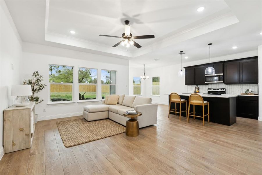 Living room featuring ornamental molding, ceiling fan with notable chandelier, light hardwood / wood-style floors, and a raised ceiling