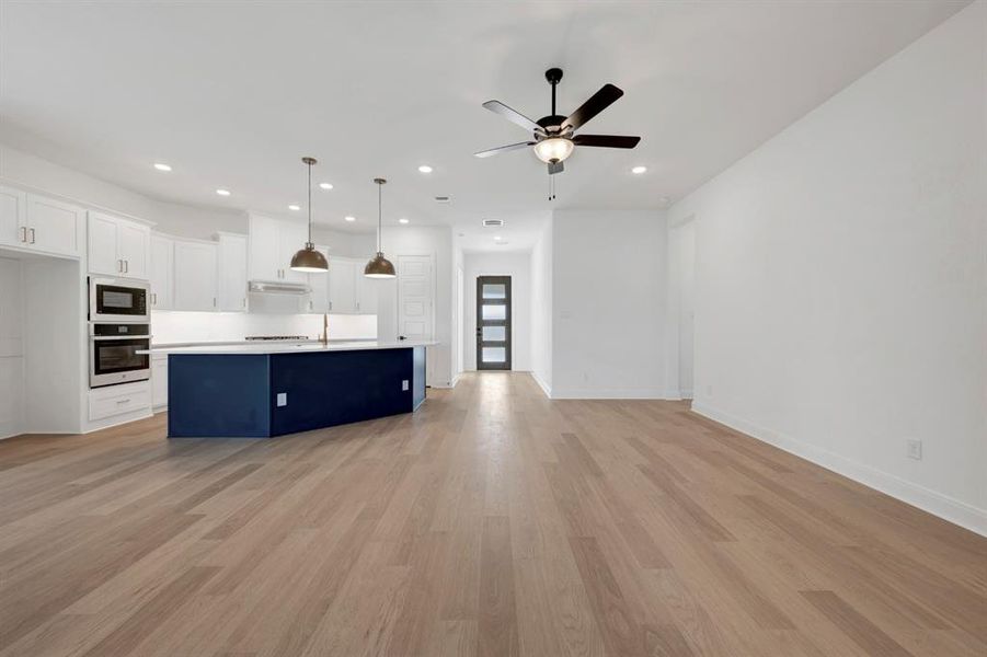 Dual tone kitchen with open floor plan, light countertops, stainless steel oven, light wood-style flooring, and a center island with sink