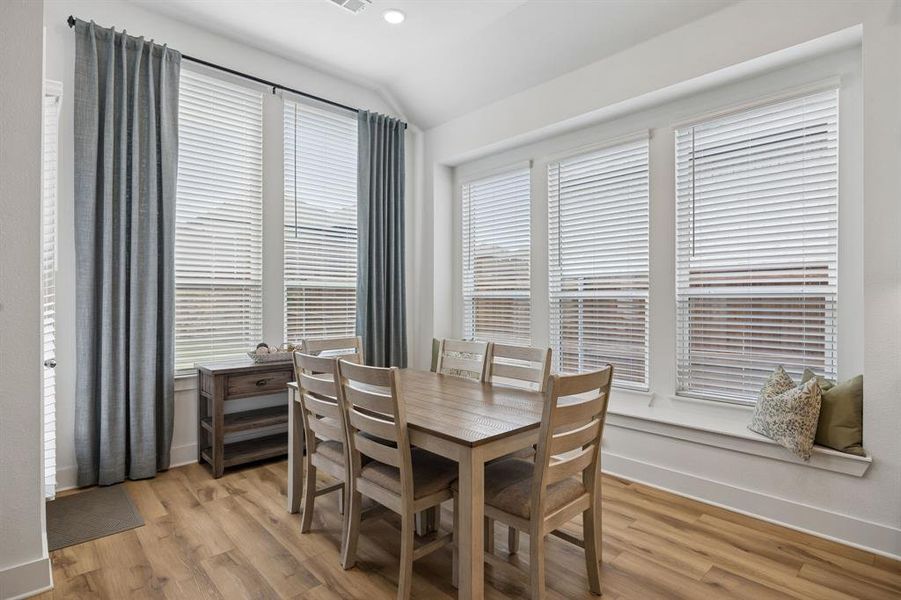 Dining area featuring wood-finish flooring, multiple large windows with blinds and drapery, and a built-in window seat