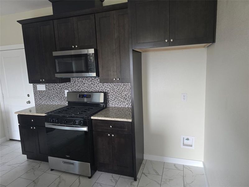 Kitchen with stainless steel appliances, light marble finish flooring, baseboards, backsplash, and light stone counters