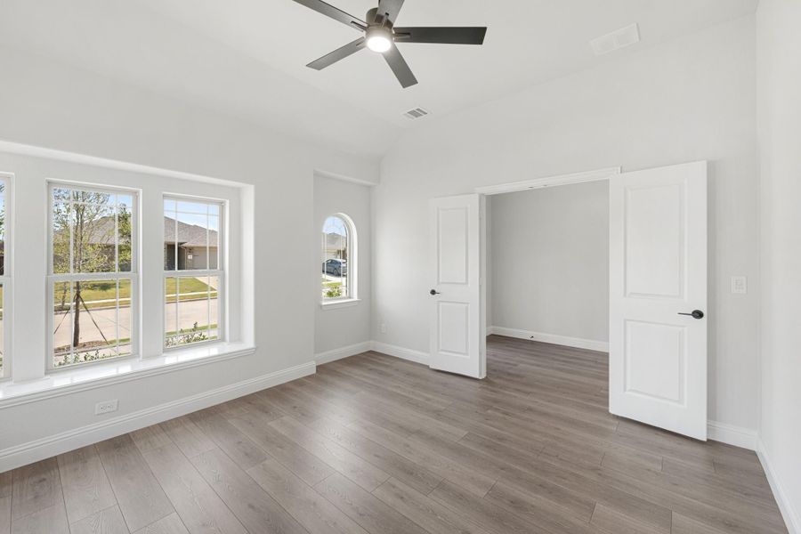 Empty bedroom with vaulted ceiling, ceiling fan, hardwood floors, and large windows overlooking a neighborhood street. Empty bedroom with vaulted ceiling, ceiling fan, hardwood floors, and large windows overlooking a neighborhood street.