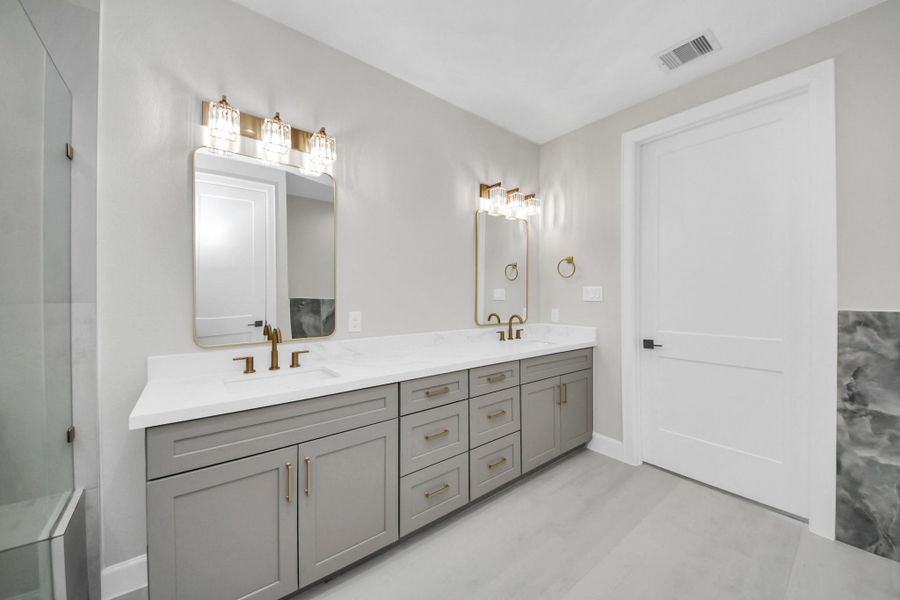 Spa-inspired primary bathroom featuring a freestanding soaking tub, oversized glass-enclosed shower, designer tile accents, and elegant gold fixtures for a true retreat experience.