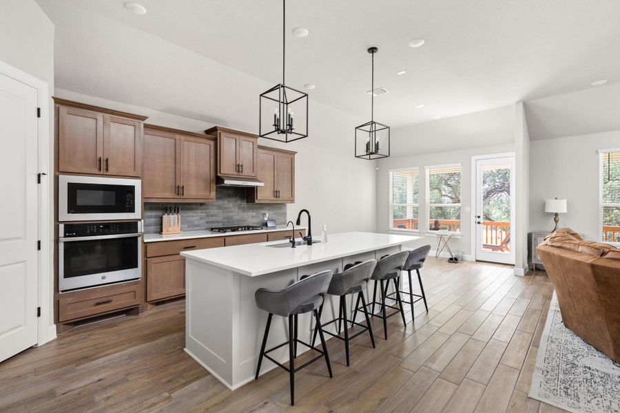Two tone kitchen featuring open floor plan, a breakfast bar, stainless steel oven, light wood finished floors, and a center island with sink