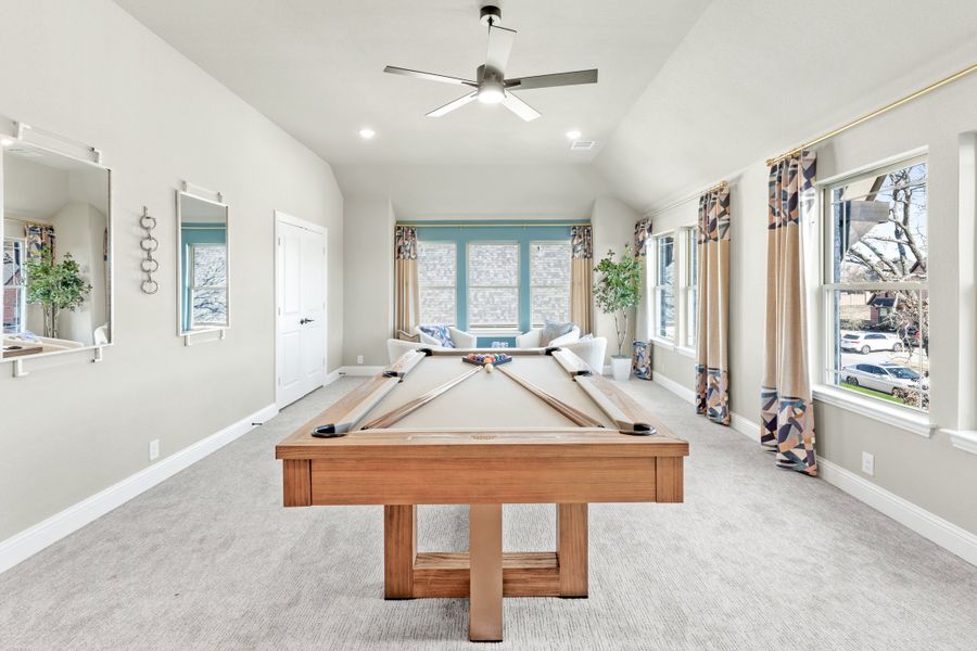 Game room with wood pool table, vaulted ceiling, ceiling fan, and large windows with patterned curtains Game room with wood pool table, vaulted ceiling, ceiling fan, and large windows with patterned curtains