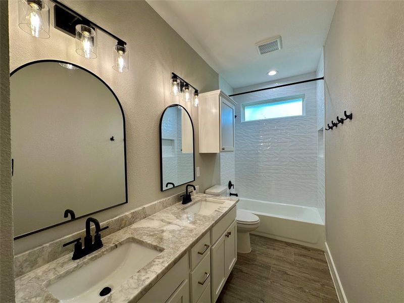 Full bathroom with double vanity, tub / shower combination, wood finished floors, and a textured wall Full bathroom with double vanity, tub / shower combination, wood finished floors, and a textured wall