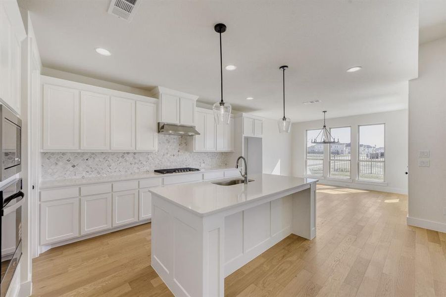 Kitchen featuring white cabinets, light wood finished floors, stainless steel appliances, and a center island with sink