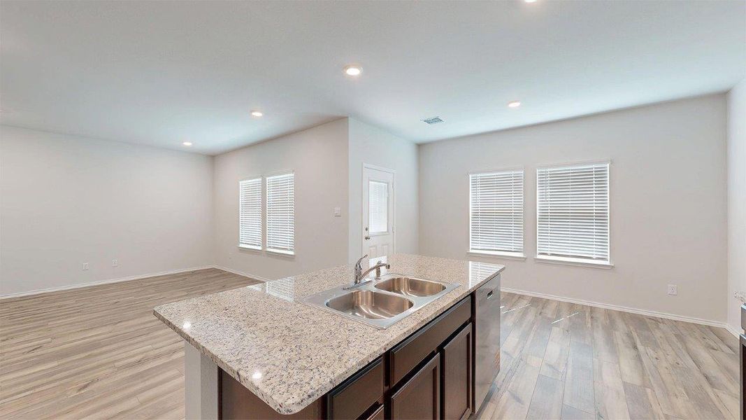Kitchen featuring dark brown cabinetry, a center island with sink, light wood-style floors, open floor plan, and light stone counters Kitchen featuring dark brown cabinetry, a center island with sink, light wood-style floors, open floor plan, and light stone counters