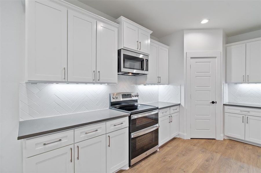 Kitchen featuring light wood-type flooring, stainless steel appliances, white cabinetry, and tasteful backsplash