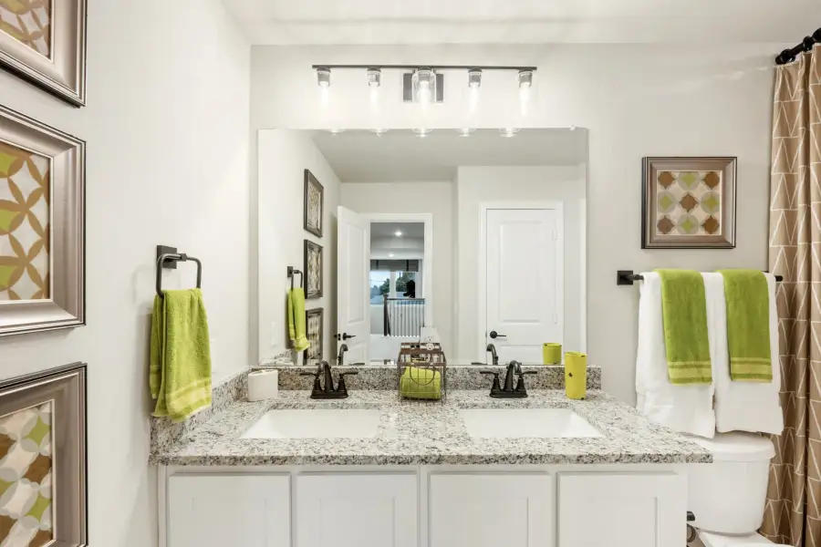 Bathroom with double sink vanity, granite countertop, white cabinets, and large mirror with overhead lighting