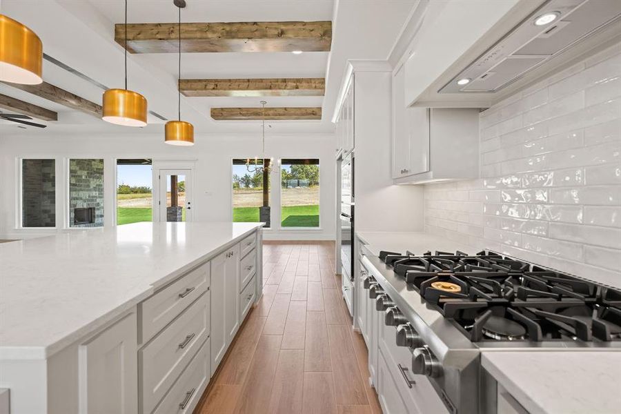 Kitchen with stainless steel appliances, white cabinetry, premium range hood, hanging light fixtures, and light stone countertops Kitchen with stainless steel appliances, white cabinetry, premium range hood, hanging light fixtures, and light stone countertops